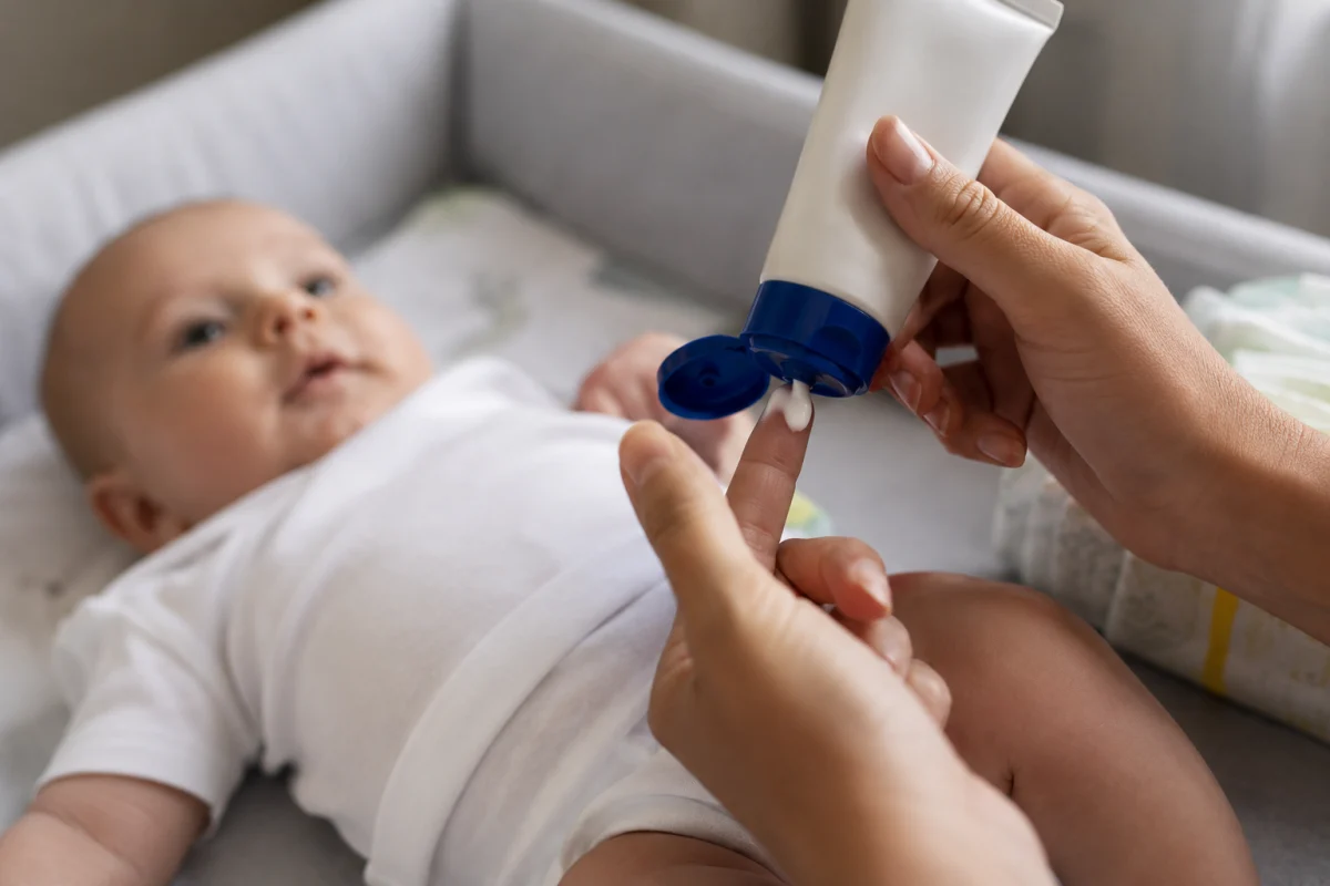 Sac à langer ouvert avec couches, crème solaire bébé et thermomètre posés sur un lit d'hôtel