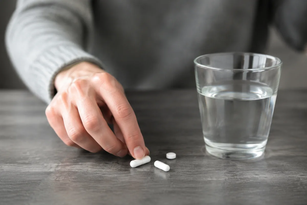 Gros plan sur une main tenant un comprimé blanc au-dessus d'un verre d'eau posé sur une table